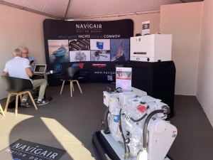 Inside Navigair's booth at Cannes Yachting Festival. Two men are talking in the corner, a model of an MTU engine is at the front.